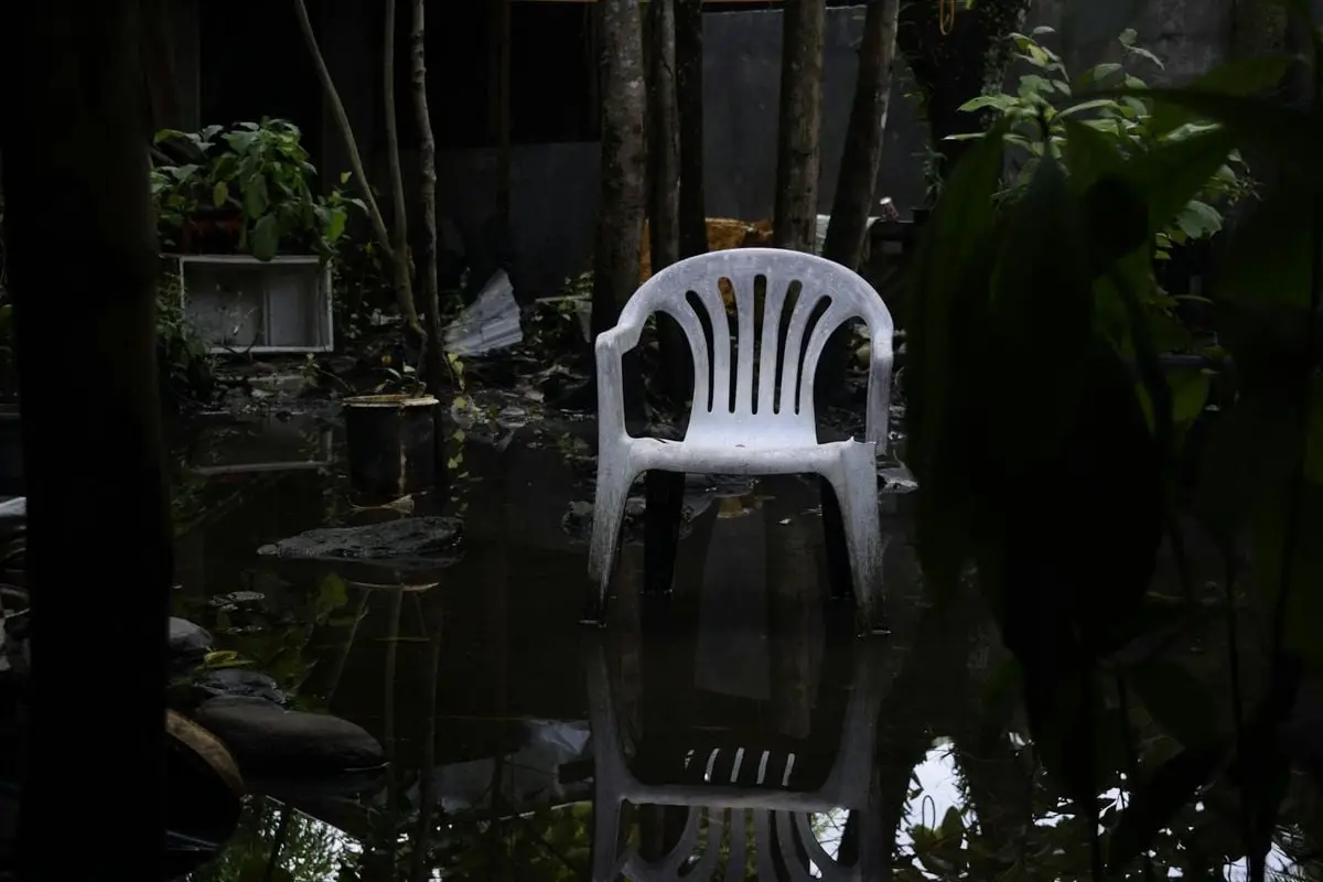 A white plastic chair reflecting in a waterlogged garden, surrounded by plants.