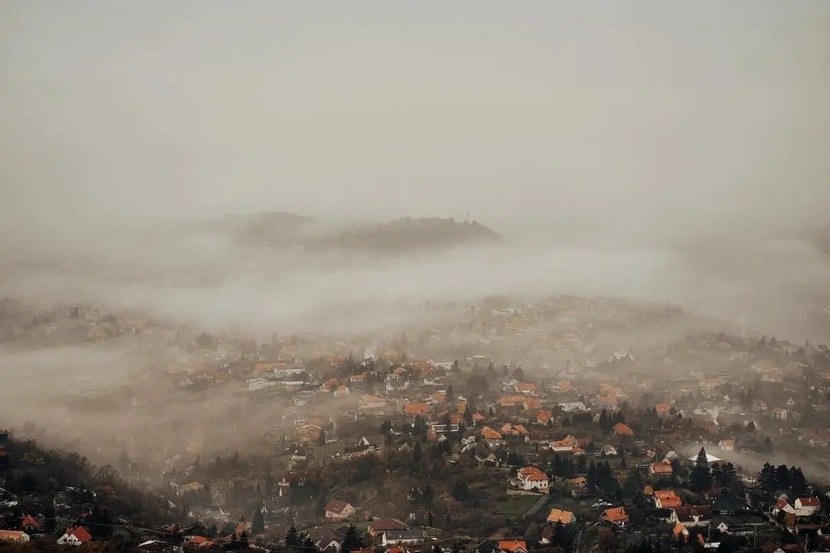 Stunning aerial view of a town enveloped in thick fog with houses peeking through, creating a serene atmosphere.