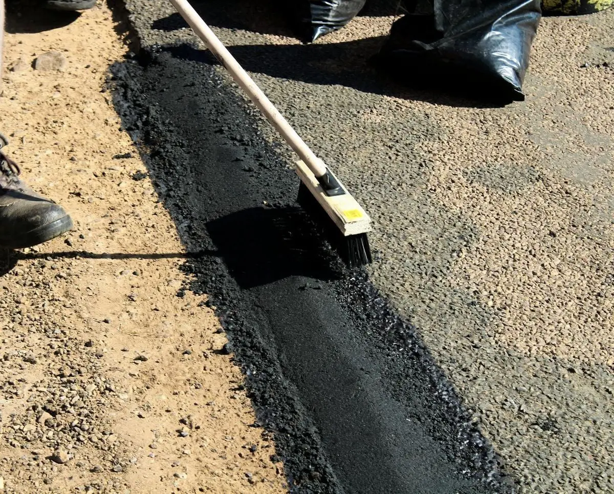 Detailed view of road maintenance with asphalt and worker tools in daytime.