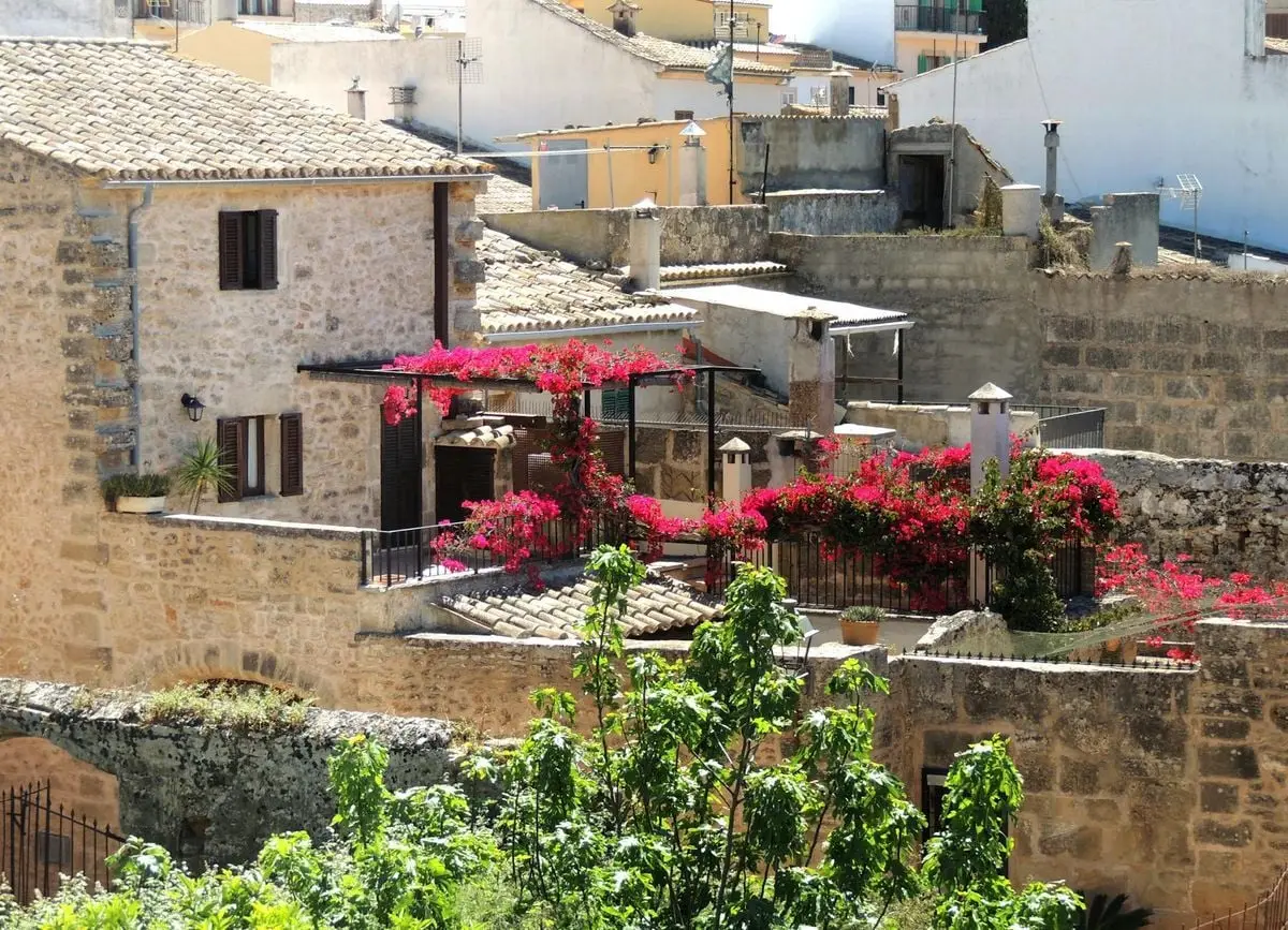 Rustic stone houses and vibrant flowers on a sunny balcony in Alcúdia, Spain.