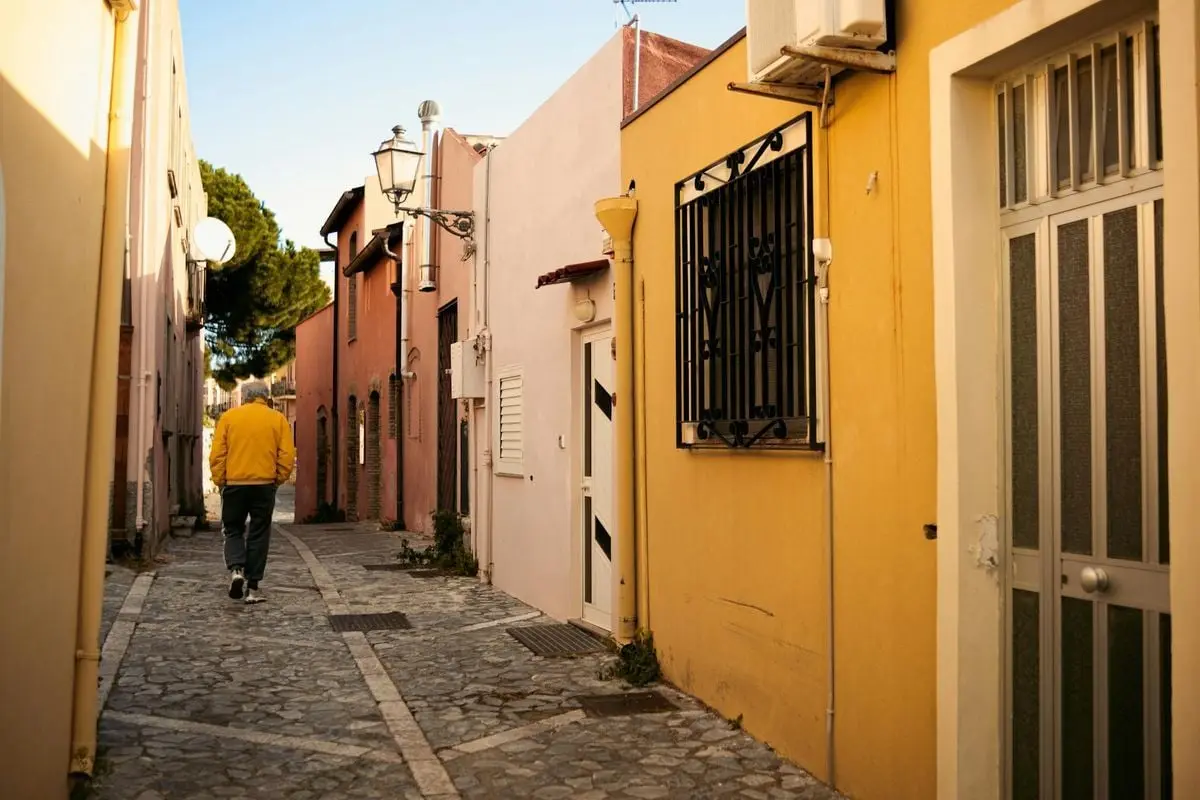 A man in a yellow jacket walks down a scenic cobblestone street in a charming urban alleyway.