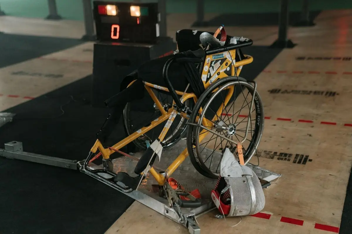 A wheelchair and fencing mask setup in a sports hall, showcasing adaptive sports equipment.