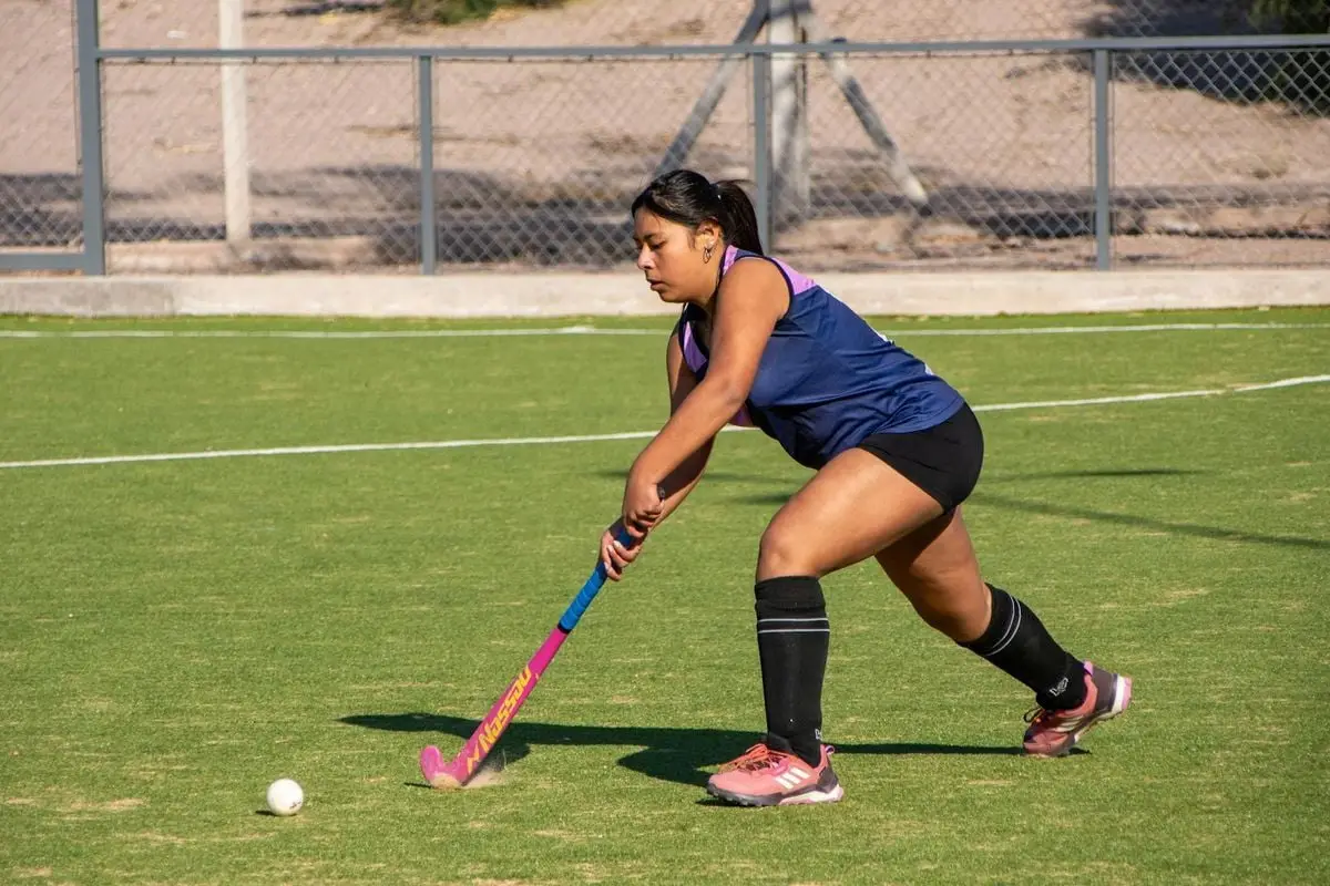 Young woman playing field hockey on green turf with determination and skill.