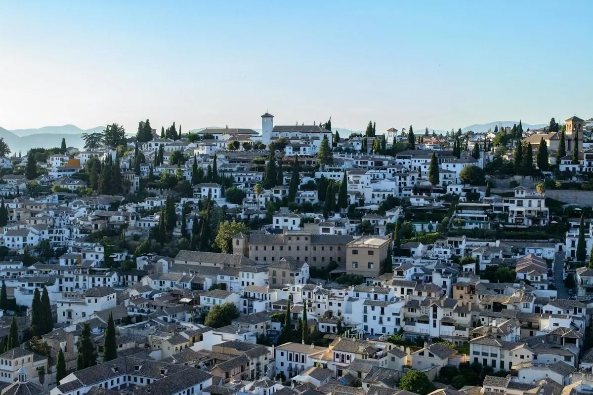 Expansive view of traditional architecture and green cypress trees in Granada, Spain.