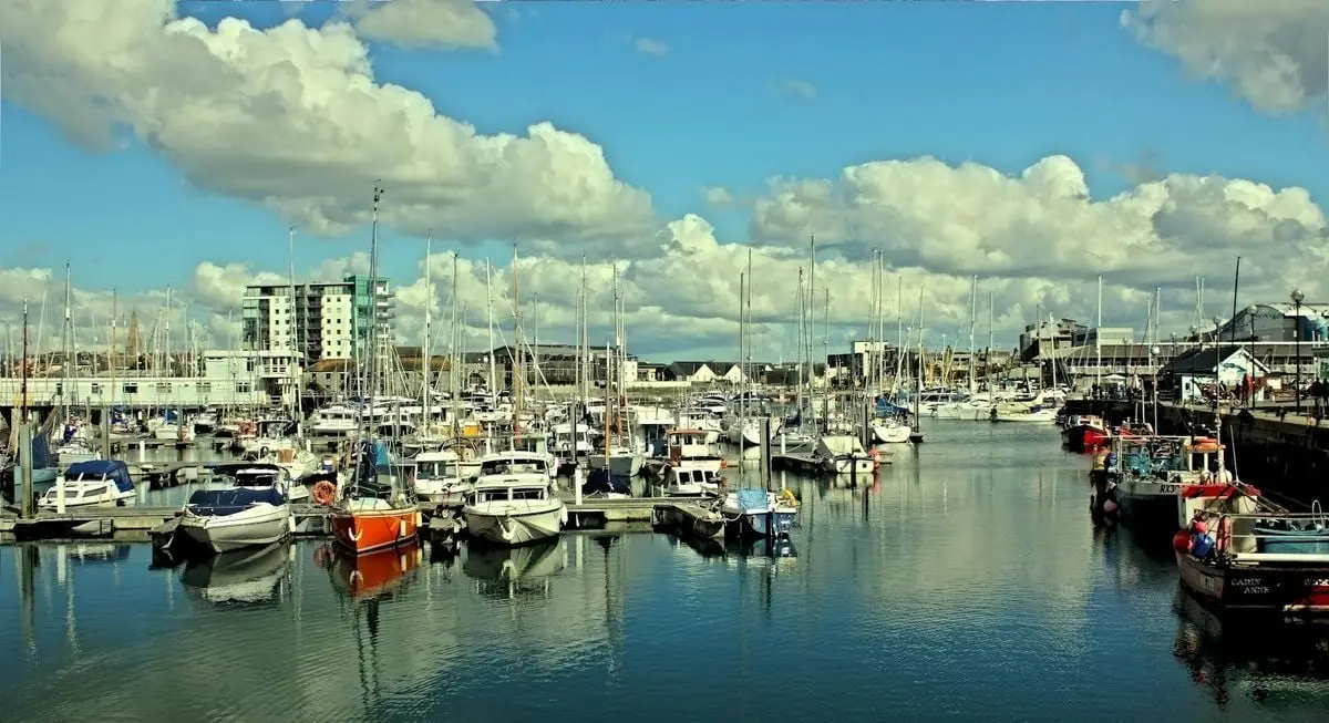 A bustling marina with various boats under a bright blue sky and clouds.