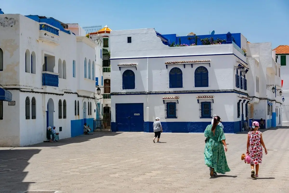 Two women walk through a picturesque Mediterranean town with iconic blue and white architecture.