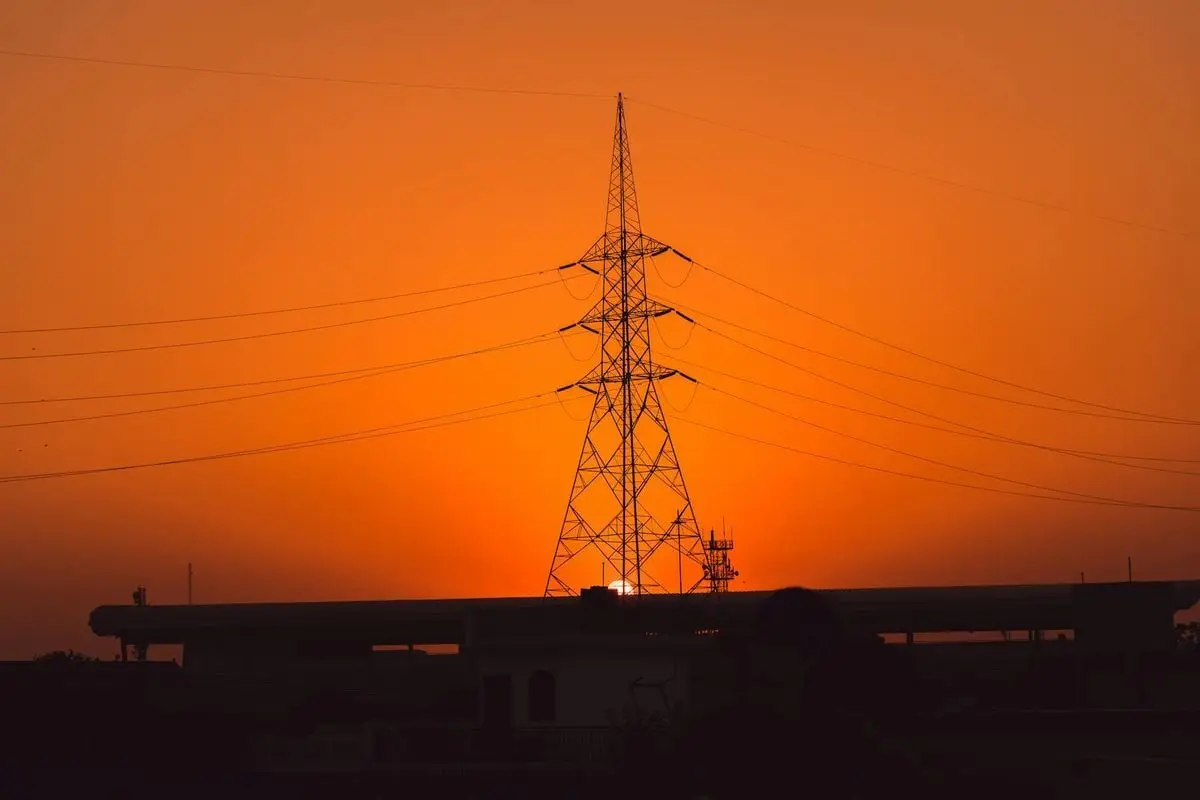 Transmission tower silhouette against an orange sunset sky, conveying energy and tranquility.