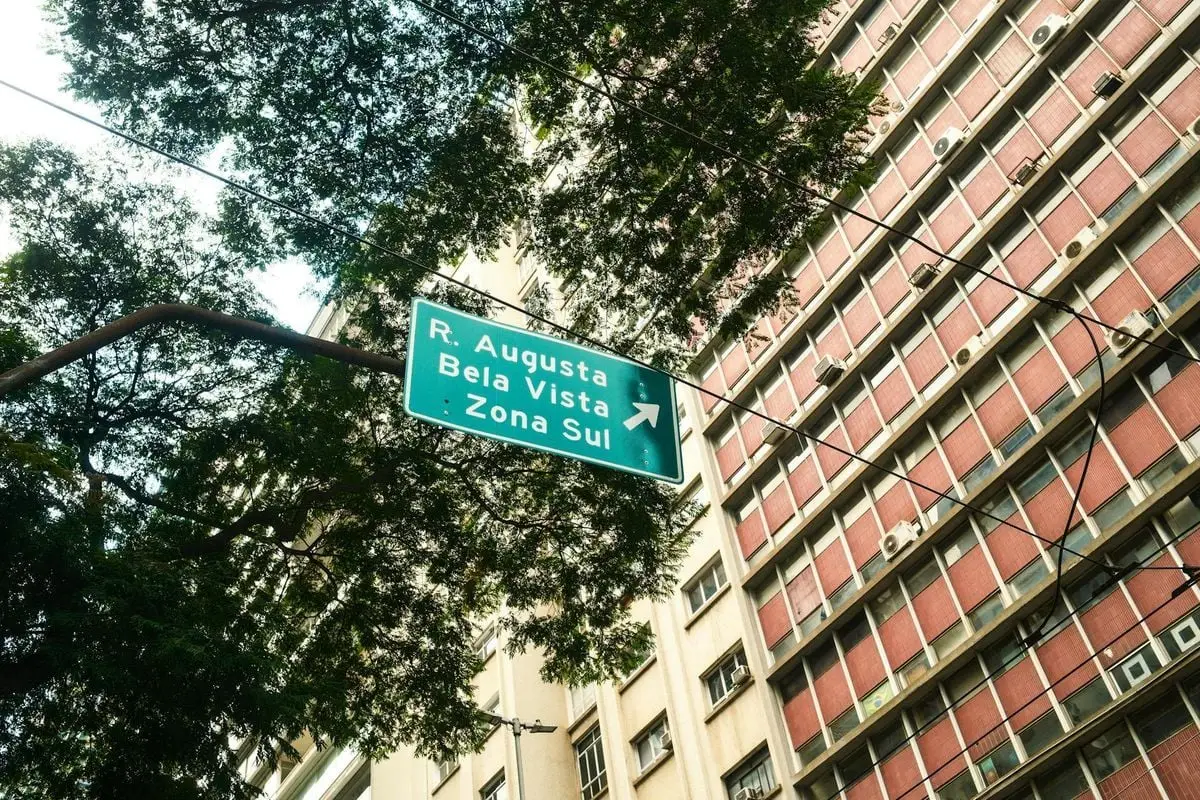 Street sign pointing to R. Augusta, Bela Vista, Zona Sul in São Paulo with urban backdrop.