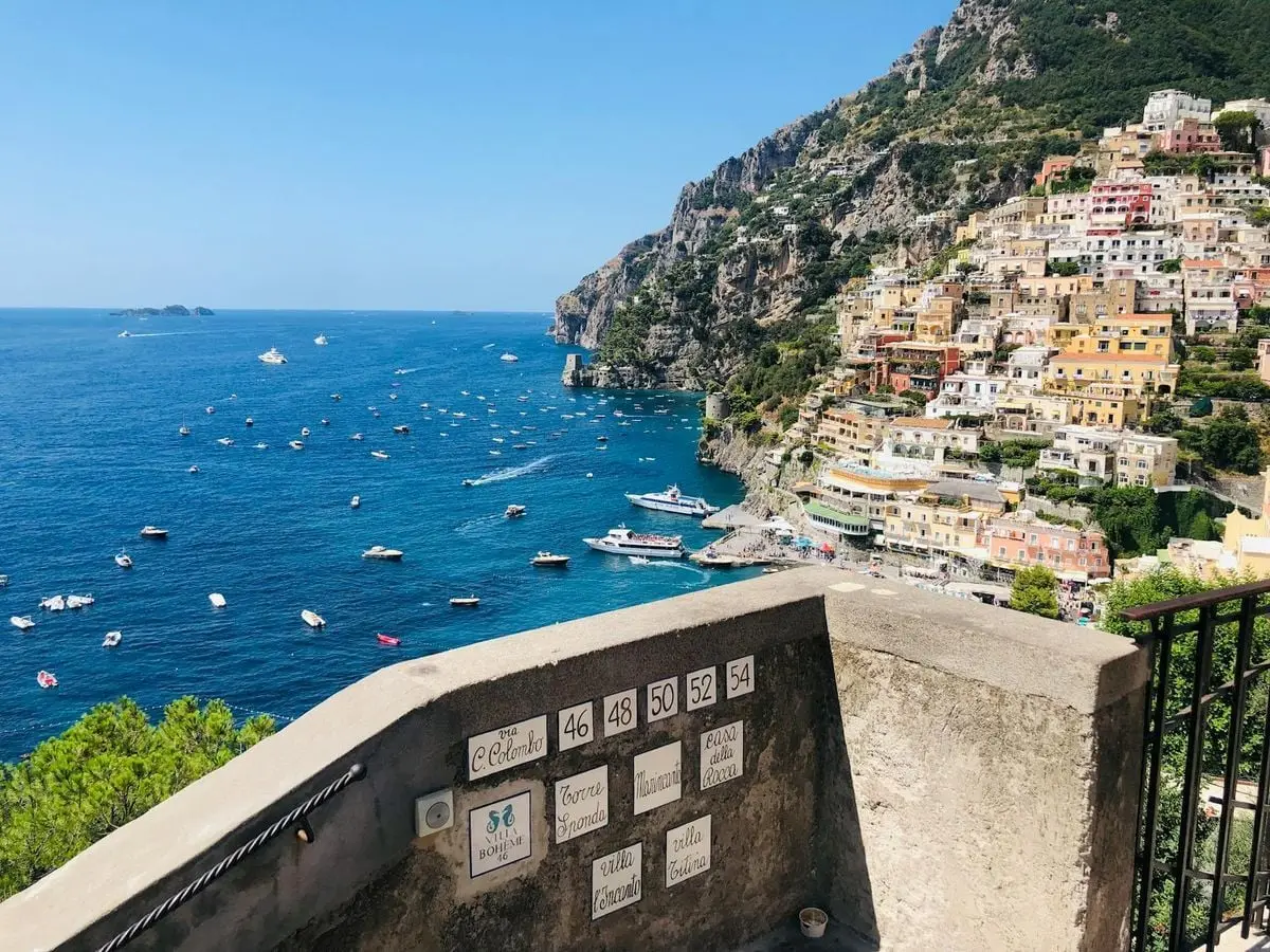 View from balcony on Positano town on tropical Amalfi coast with boats sailing at sea on sunny day
