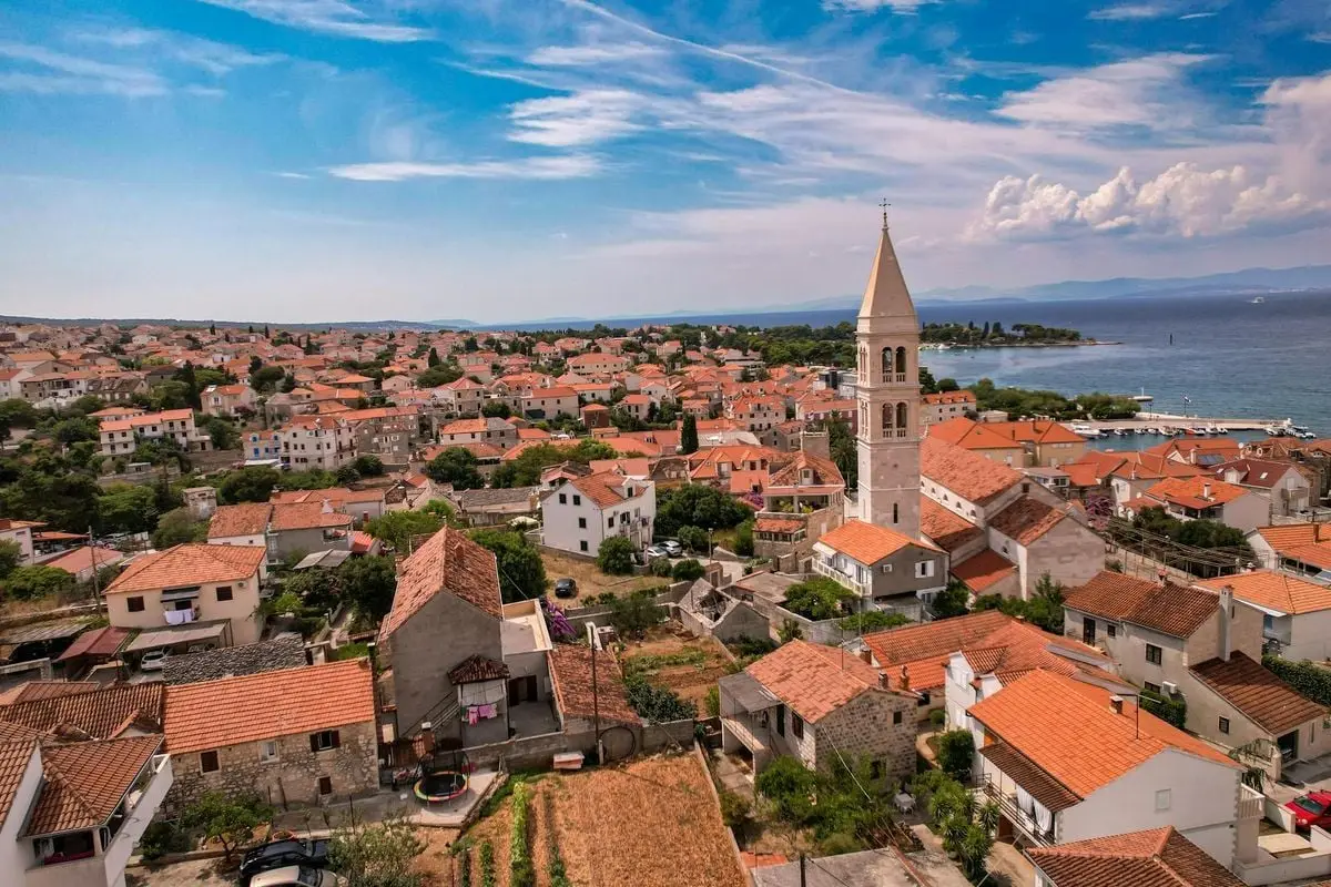 Aerial view of a charming coastal town with a historic church tower and red-roofed houses next to the sea.