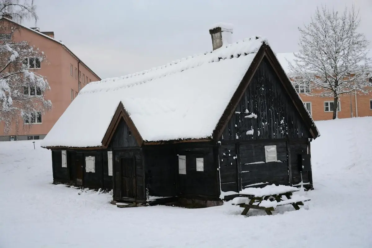 A charming rustic cabin covered in snow during winter, surrounded by snow-covered trees.