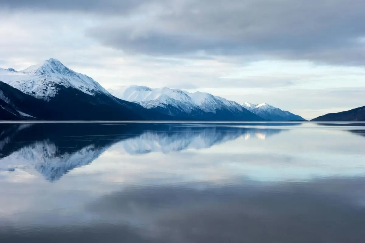 Beautiful snow-capped mountains reflected in a calm lake under a cloudy sky, evoking a tranquil winter landscape.