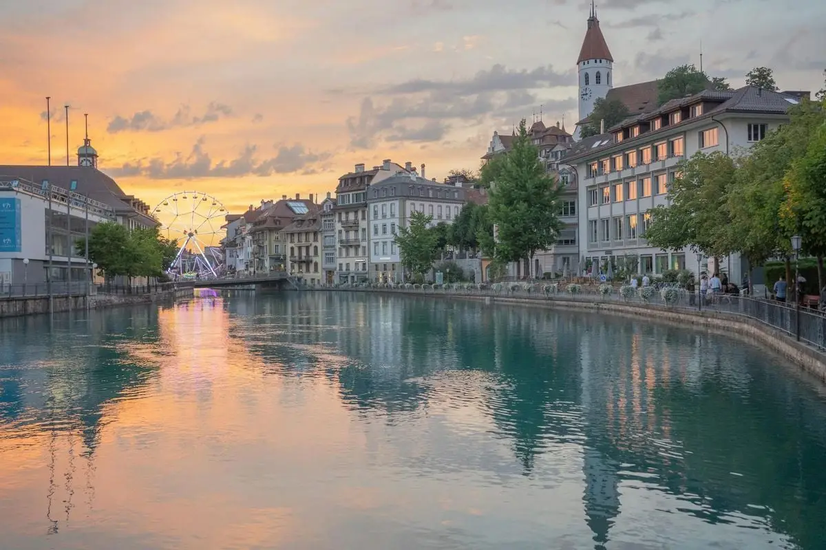 Beautiful sunset view of Thun with cityscape reflections on the river and a Ferris wheel.