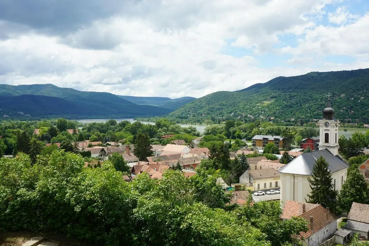 A picturesque aerial view of Visegrád, Hungary featuring a church, rooftops, and lush mountains.