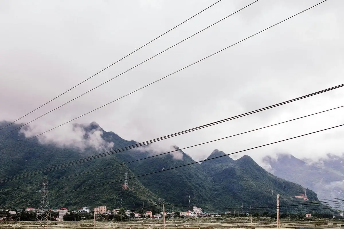 Scenic view of a foggy mountain town with power lines and cloudy skies in the countryside.