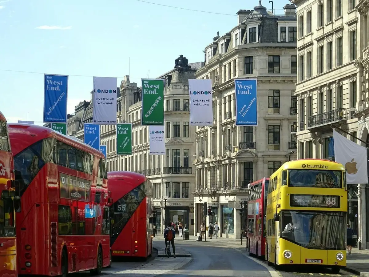 Street view of London's West End featuring iconic red double-decker buses and classic architecture.