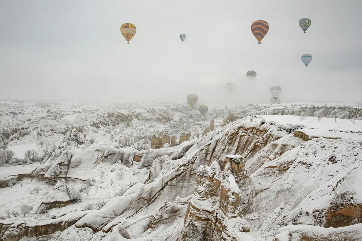 Hot air balloons glide over Cappadocia's snowy landscape, creating a breathtaking winter scene in Turkey.