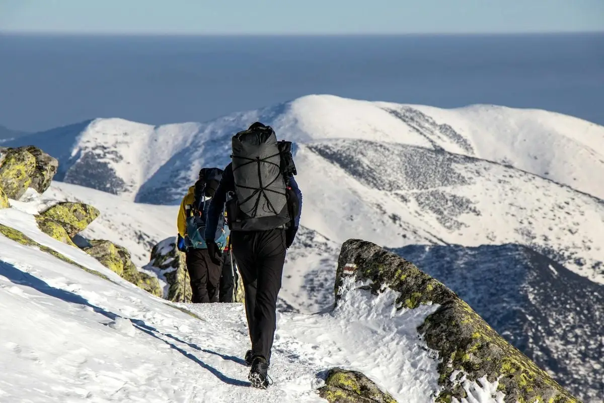 Hikers with backpacks trek through snow-covered mountains on a sunny winter day.