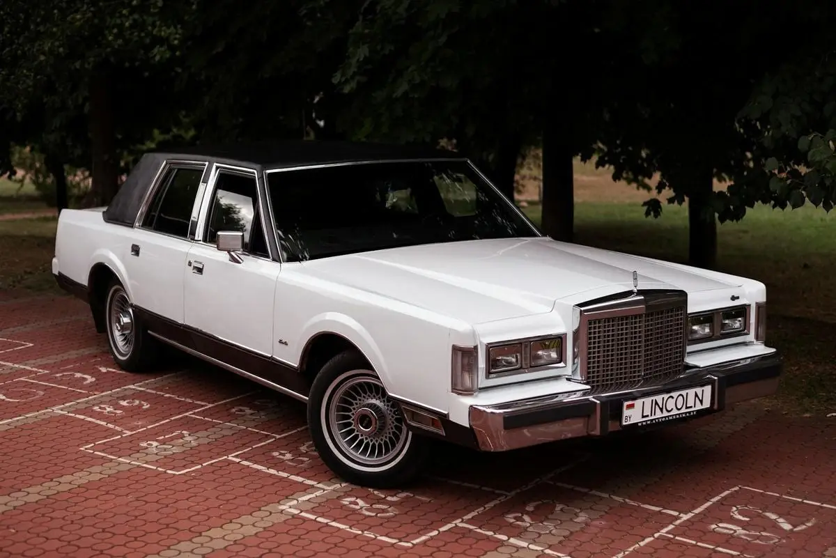 Vintage Lincoln Town Car parked on a brick pavement amidst greenery.