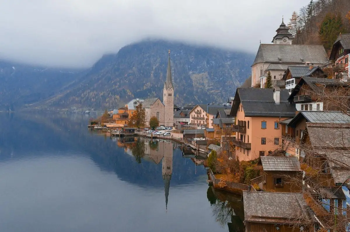 Stunning view of Hallstatt, Austria with a church, calm lake, and misty mountains.