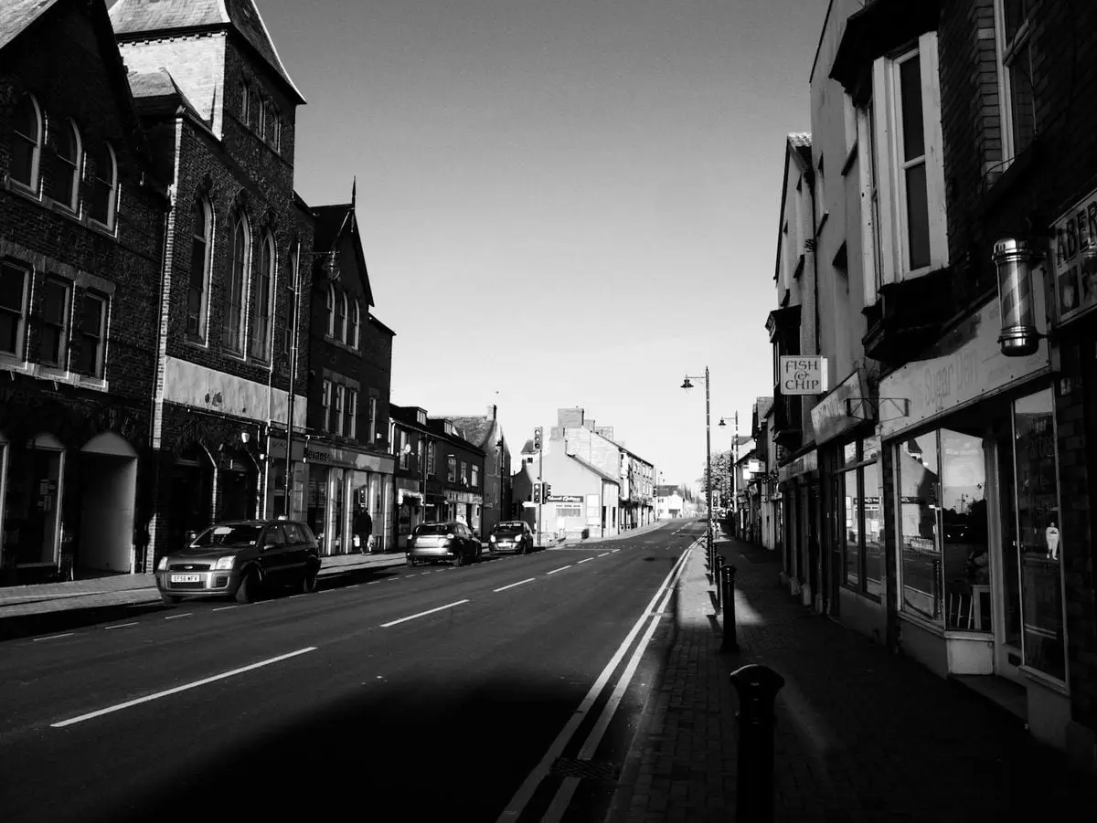 A monochrome view of an empty city street lined with historic buildings and parked cars.