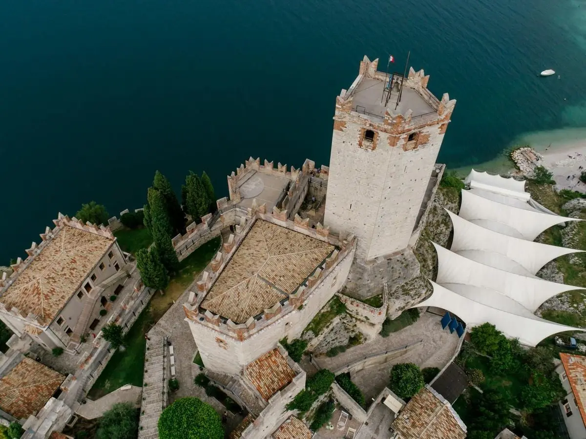 Aerial view of a medieval tower and nearby structures by a serene lake.