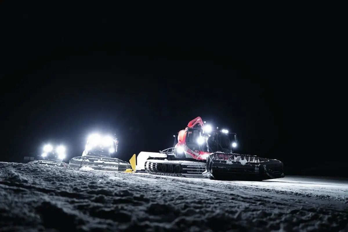 Illuminated snow groomers working at night in Zermatt, Switzerland during winter.