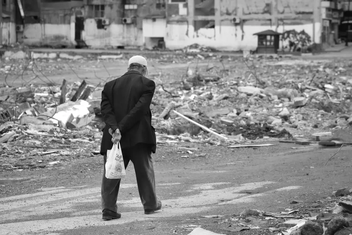An elderly man walks through urban ruins, depicting the aftermath of destruction.