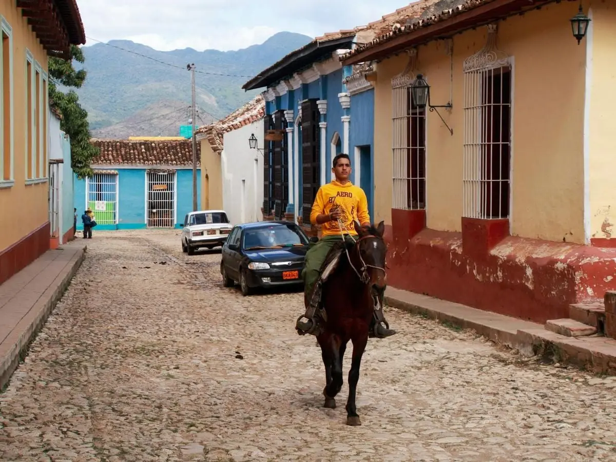 Man riding a horse through a colorful cobblestone street in a Latin American town, captured during the day.