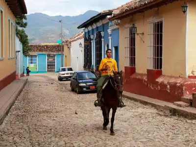 Man riding a horse through a colorful cobblestone street in a Latin American town, captured during the day.