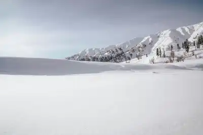 Winter landscape of snow-covered mountains in Gulmarg, Kashmir under clear skies.