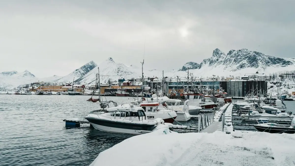 A serene snowy harbor with fishing boats docked, set against the backdrop of snow-covered mountains in Arctic Norway.