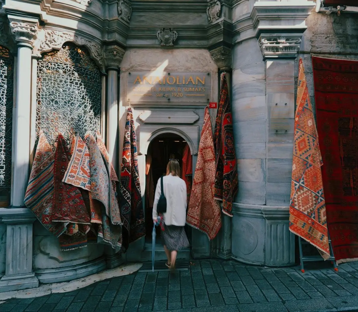 A woman enters a traditional carpet store in Istanbul, displaying vibrant Anatolian rugs.
