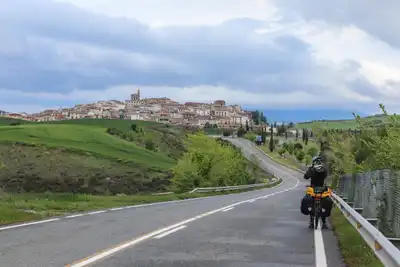 Breathtaking view of a cyclist on a winding road approaching a Spanish hilltop town under a moody sky.