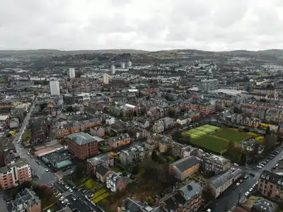Aerial view of a picturesque town in Scotland, showcasing architecture and landscape amidst cloudy skies.