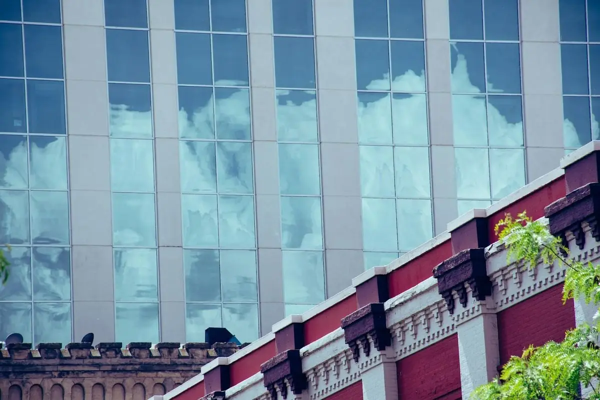 Glass facade reflecting clouds against a decorative urban building.