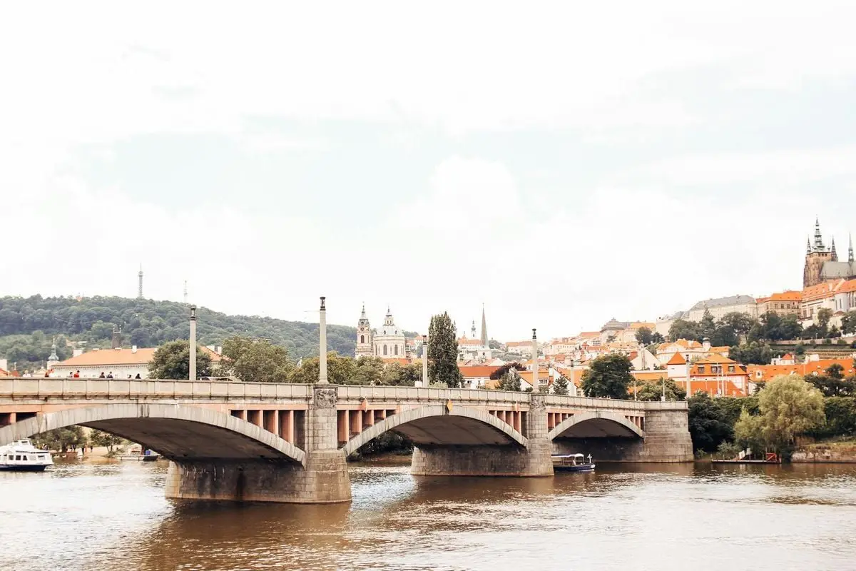 Scenic view of a historic bridge over Vltava River with Prague's cityscape in the background.