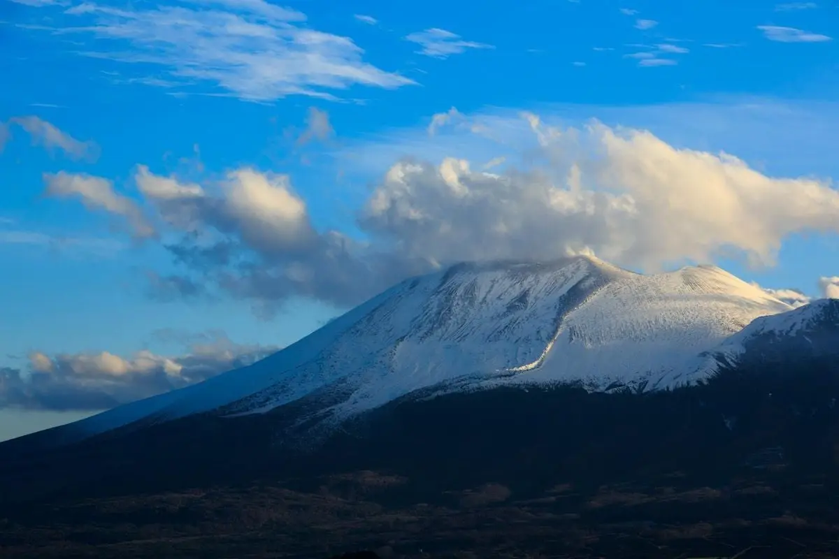 Mesmerizing view of Mount Asama with snow, clouds, and blue sky, creating a picturesque landscape.