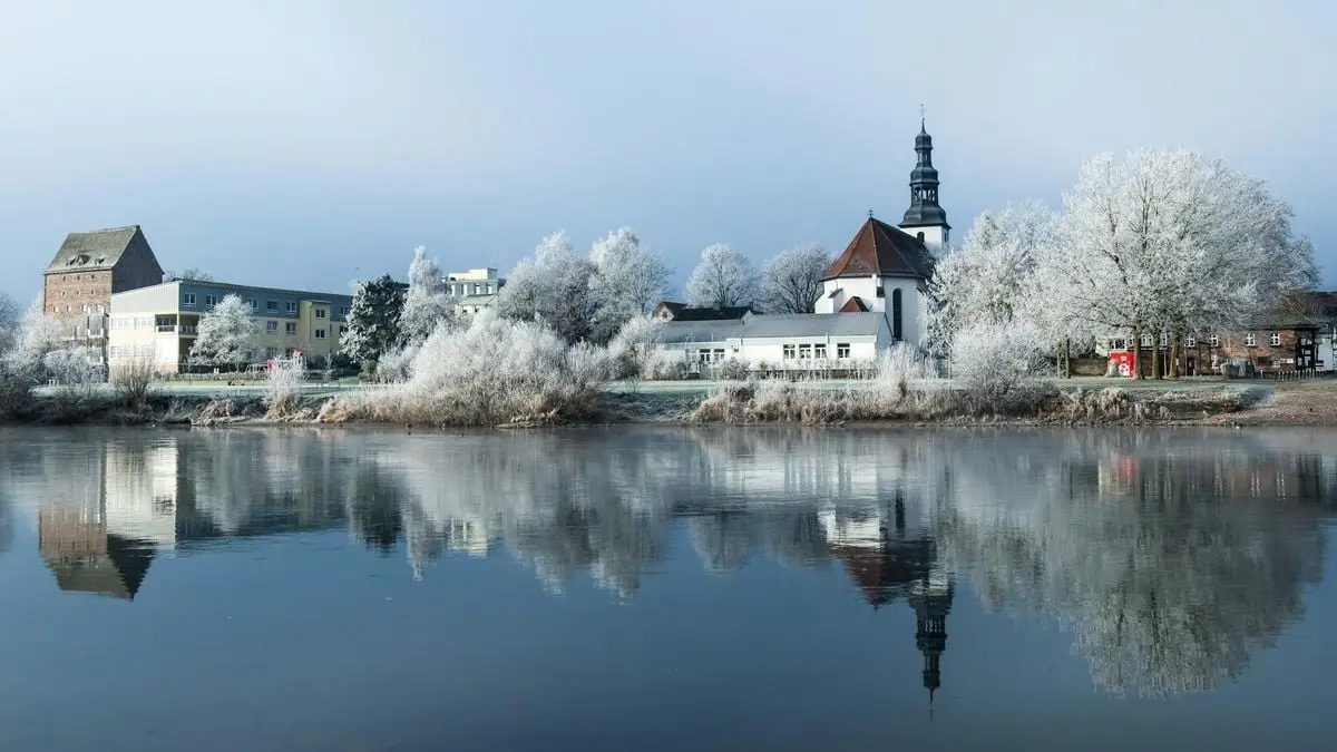 Peaceful winter view of Beverungen, Germany with a church and lake reflection.