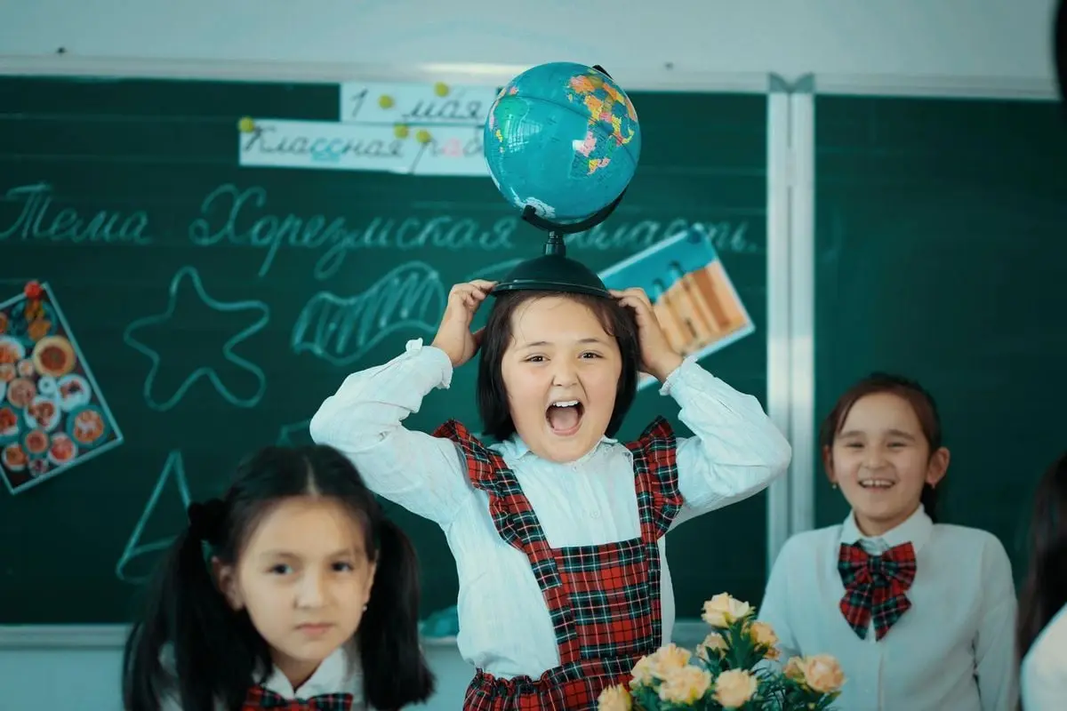 Joyful kids in a classroom exploring education with a globe in Andijan, Uzbekistan.