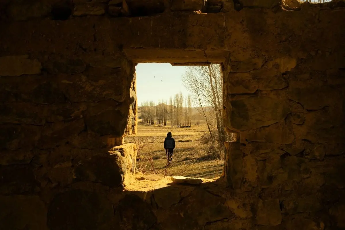 A person walks in a rural landscape seen through an ancient stone window.