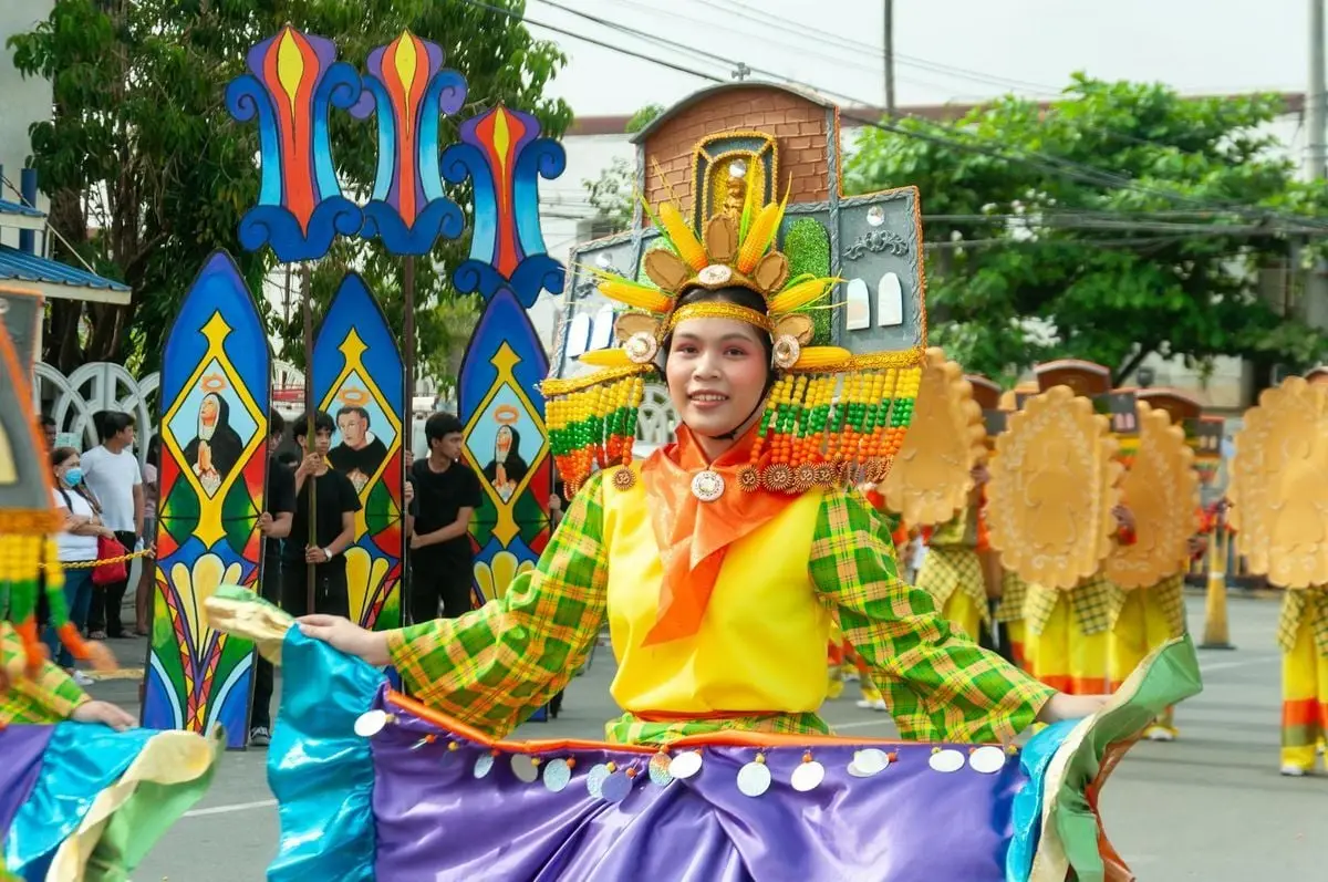 Energetic dancers in vibrant costumes perform at a lively street festival parade with colorful decorations.