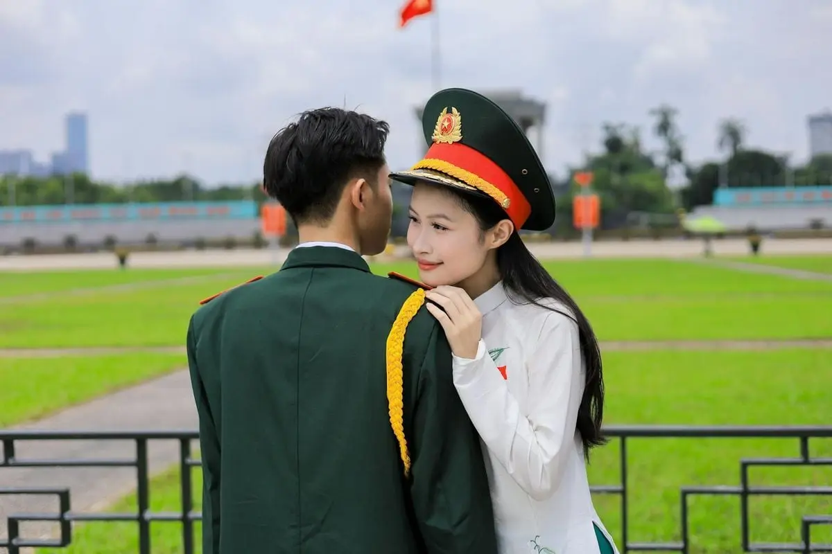 A tender moment between a Vietnamese military couple in uniform outdoors, symbolizing love and duty.