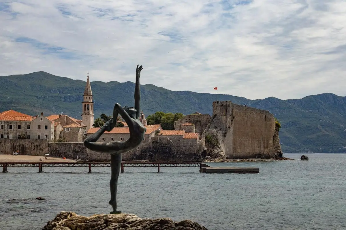 A picturesque scene of Budva Old Town with the famous dancer statue and the Adriatic Sea.