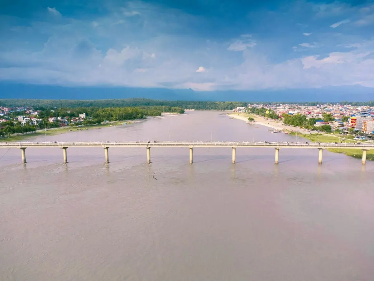 A serene aerial view capturing a long bridge over a calm river, adjacent to a small town, under a clear sky.