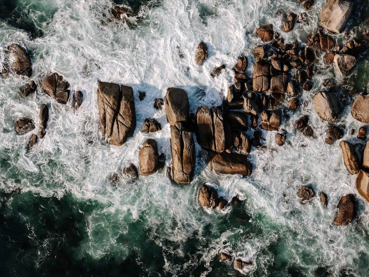 Stunning aerial view of ocean waves crashing onto rocky Cape Town shoreline.