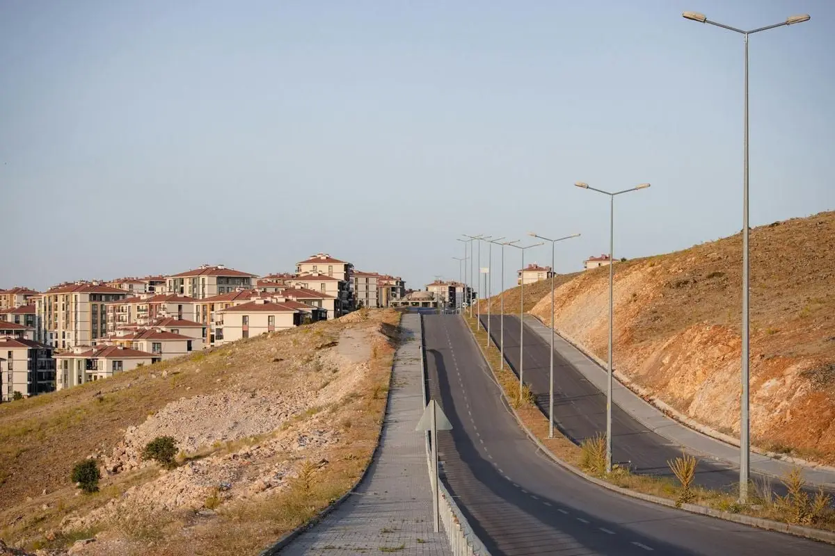 A modern urban landscape with a road winding through newly constructed apartment buildings under a clear sky.