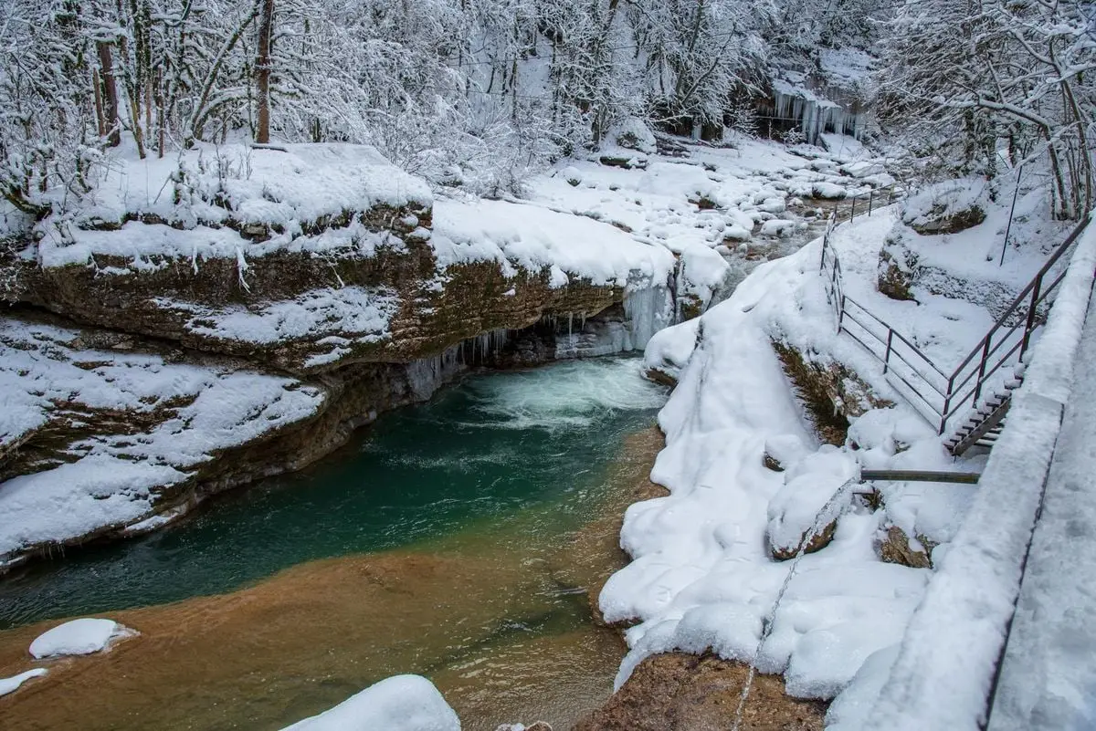 A picturesque winter river scene with snow-covered rocks and flowing water in a forest.