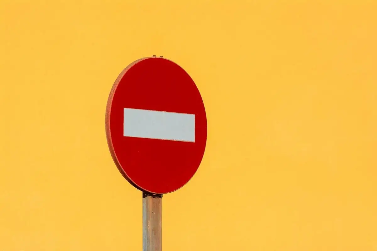 Red no entry sign on pole against bright yellow wall, symbolizing restriction and caution.