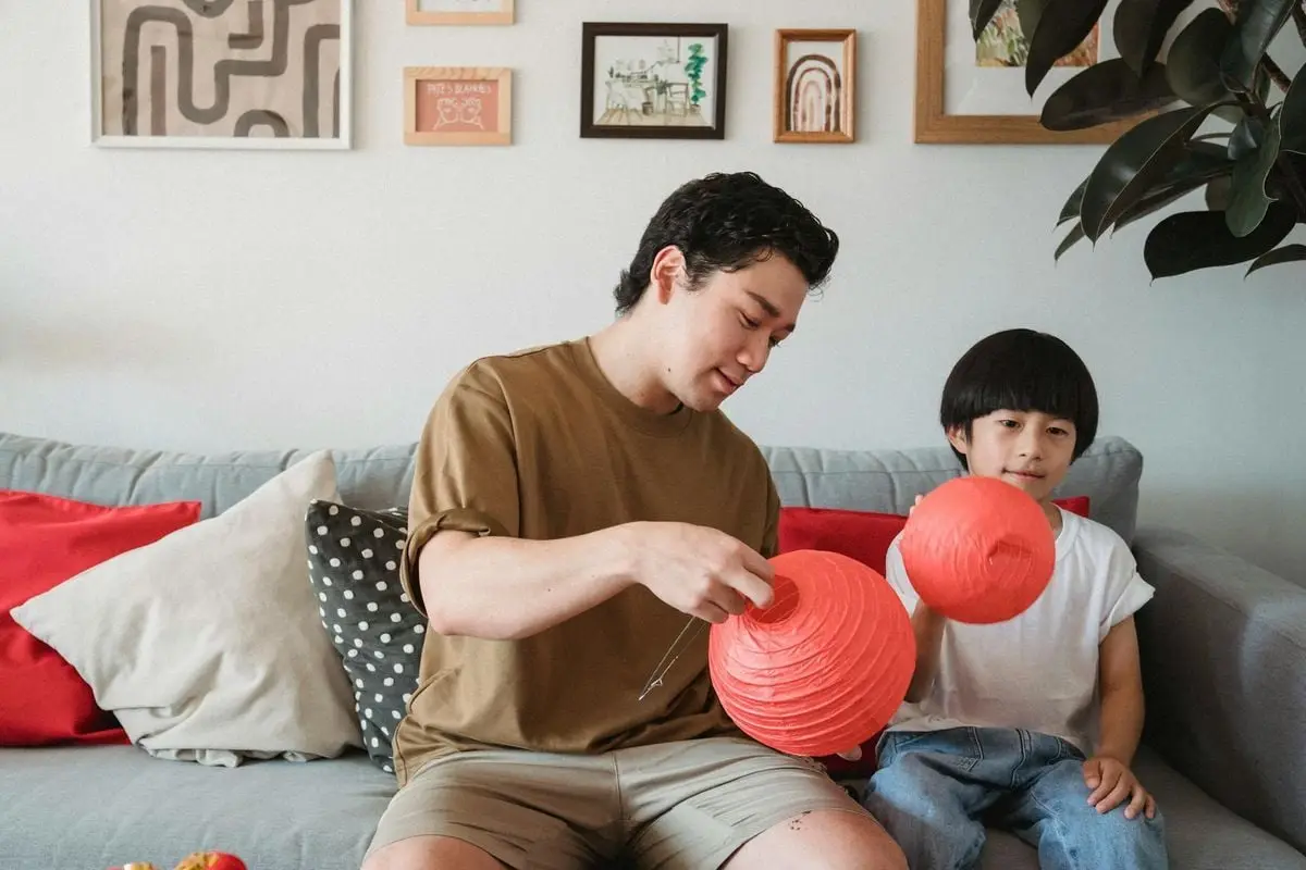 A father and son enjoying quality time decorating with lanterns in a cozy living room.